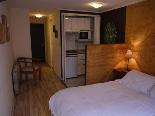 um quarto com uma cama branca e uma cozinha em Encomenderos Suites - Apartamentos Amoblados em Santiago
