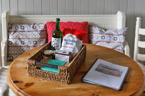 a basket with a bottle of wine and other items on a table at Finest Retreats - The Stables at Crimplesham in Stradsett