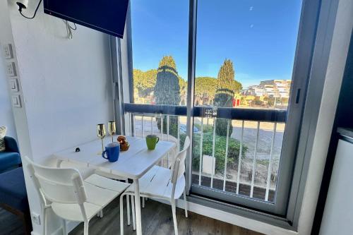 une table blanche et des chaises dans une pièce avec une fenêtre dans l'établissement LE CABESTAN - studio proche plage, au Grau-du-Roi