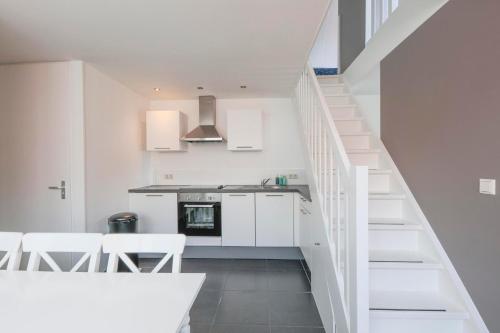 a kitchen and dining room with white cabinets and stairs at Weststraat 22 - Ouddorp - Appartement West 3P in Ouddorp