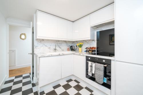 a kitchen with white cabinets and a checkered floor at Niru Experience Stylish Garden Getaway in London