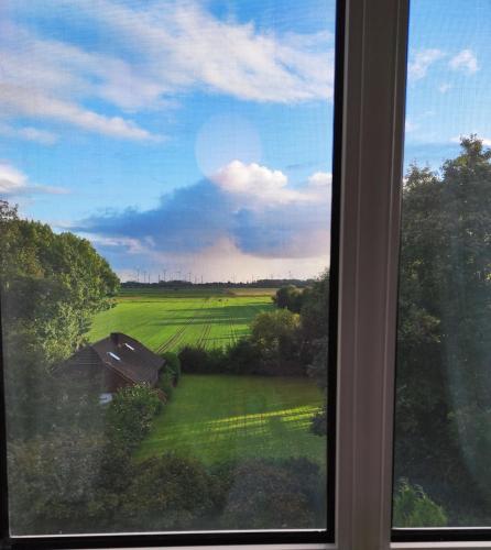 a window with a view of a green field at FeWo Nesthäkchen-Erholung in Historischer Villa an der Nordsee in Dornum