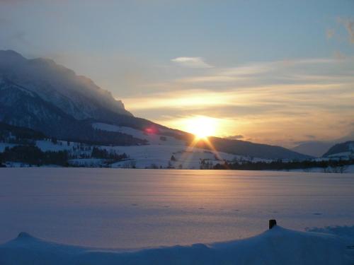 a sunset over a snow covered lake in the mountains at Mountain Inn Chalets & Apartments in Walchsee