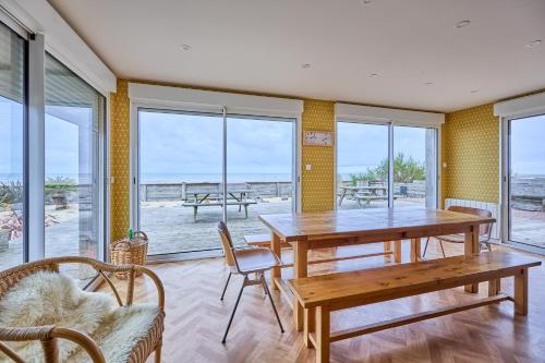 une salle à manger avec une table, des chaises et des fenêtres dans l'établissement La Villa des Marées - Front de mer, à Asnelles