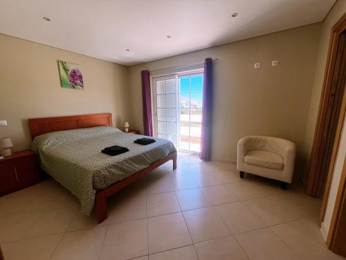 a bedroom with a bed and a chair and a window at Moradia Fantástica com Piscina a 5 min da Praia in Monte Gordo
