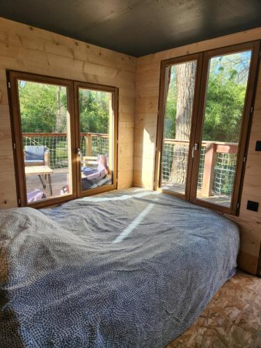 una camera da letto con un letto in una stanza con finestre di La cabane des bords d'Ariège a Grépiac