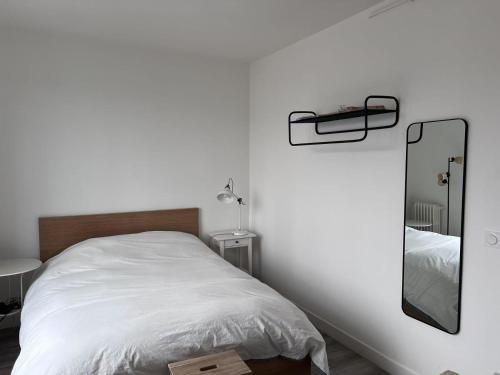 une chambre blanche avec un lit et un miroir dans l'établissement Studio Plein Soleil Seine, à Paris