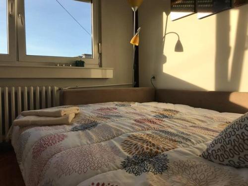 a bed with a comforter on it with a window at Bright and cozy room in the city centre in Novi Sad