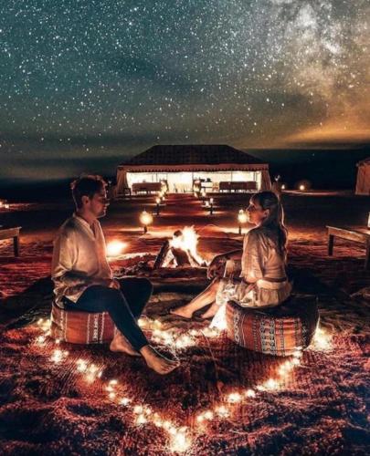 a man and a woman sitting around a fire at night at Merzouga Sara Luxury Camp in Merzouga