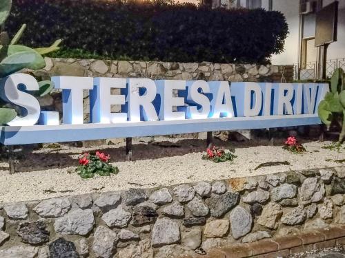 a sign on a stone wall with some flowers at CasaBlanc in Santa Teresa di Riva