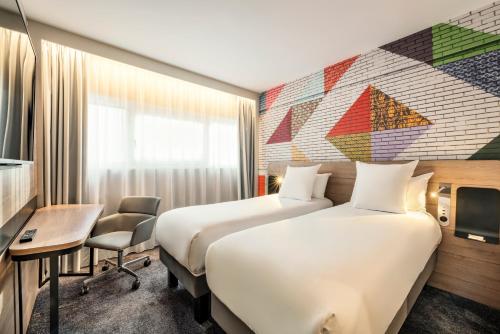 a hotel room with two beds and a desk at Novotel Paris La Défense Nanterre in Nanterre