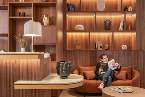 a man sitting on a couch reading a book at Novotel Paris La Défense Nanterre in Nanterre