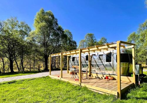 ein Haus mit einer Holzterrasse auf einem Feld in der Unterkunft Bonny Airstream in Inver Mallie