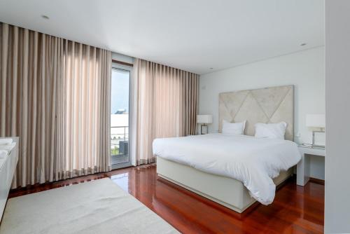 um quarto com uma cama branca e uma janela grande em The Povoa Villa na Póvoa do Varzim