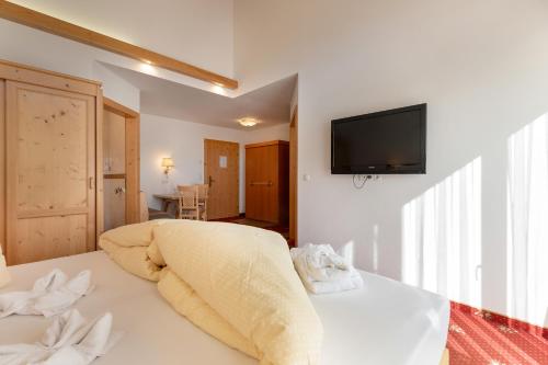 a white room with a bed with a television on the wall at Hotel Pinzger Tux in Tux