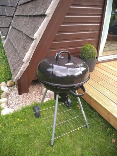 a grill sitting in the grass next to a house at True North Lodge - A cosy wee highland Getaway in Spean Bridge