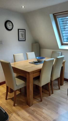 a dining room table with white chairs and a clock at True North Lodge - A cosy wee highland Getaway in Spean Bridge