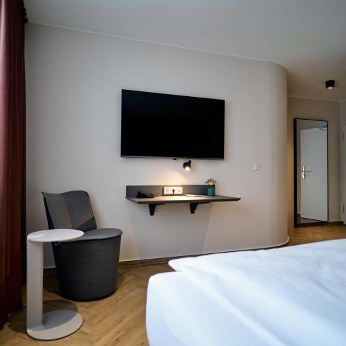 a bedroom with a tv on the wall and a chair at Hotel Engbert in Oelde