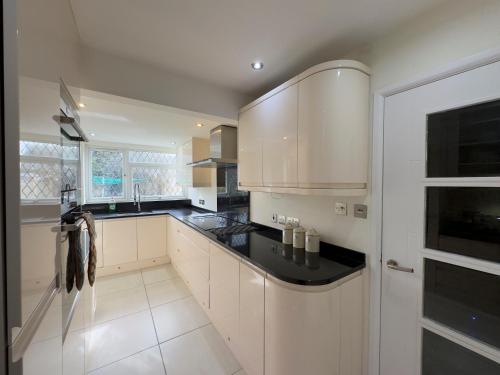 a kitchen with white cabinets and black counter tops at Cosy Guest House, Langley, Slough in Langley Station