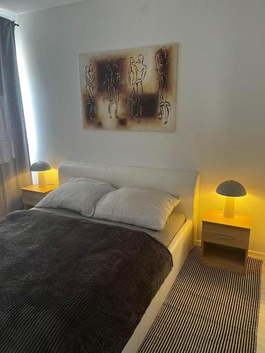 a bedroom with a bed and two lamps and a painting at 3 Barát Apartman in Kehidakustány