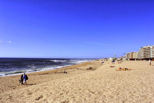 a beach with people laying on the sand and the ocean at Guest House da Mata2 in Póvoa de Varzim
