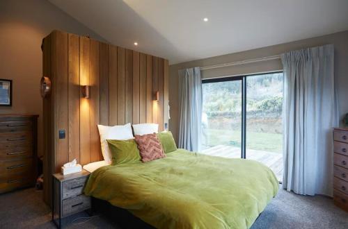 a bedroom with a green bed with a large window at Bobs Cove Nature Getaway and spa in Mount Creighton