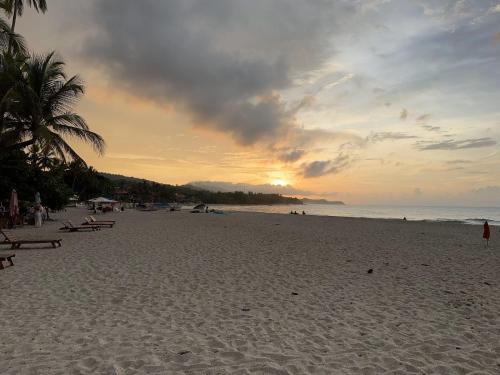 a beach with a sunset and people on the sand at Puerto Manglar Hostal in Guachaca