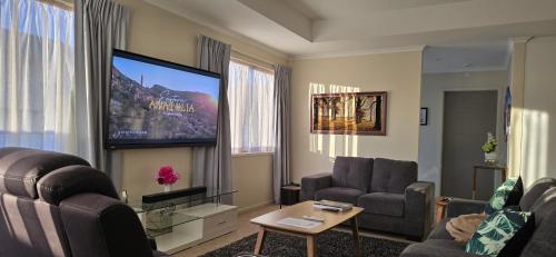 a living room with a tv and a couch and chairs at 3 Bedroom home in Palmerston North with BBQ and Sky Tv in Palmerston North
