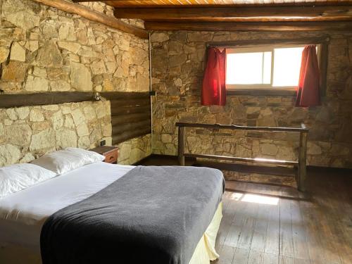 a bedroom with a bed and a window in a stone wall at Cabañas Cuyum in El Volcán