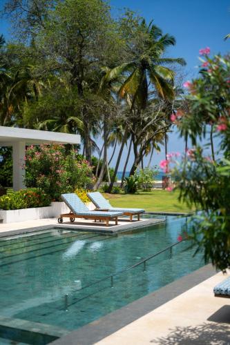 a pool with two lounge chairs and palm trees at Kalkudah Beach House in Batticaloa
