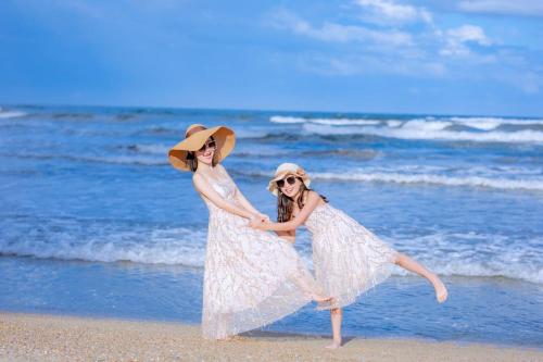 two girls in white dresses dancing on the beach at Dusit Thani Shuangyue Bay Resort Huizhou in Huidong