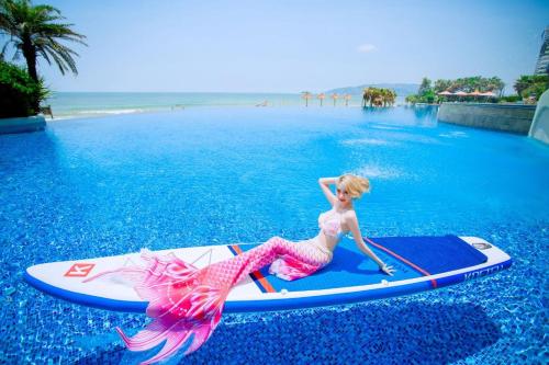 a woman in a pink dress on a surfboard in the water at Dusit Thani Shuangyue Bay Resort Huizhou in Huidong