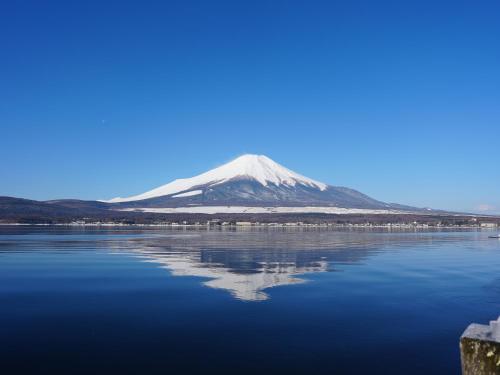 a mountain reflecting in the water in front of a lake at Mt Fuji View and Private Sauna Ryokan Shizuku in Yamanakako