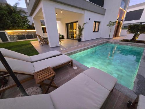 a swimming pool with chairs and a house at TG NEW Luxury Private Resort & SPA Villas - Heated Salty Swimming Pool, Outdoor Jacuzzi, Sauna, Exotic Garden in Limassol