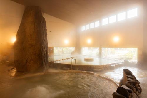 a large hot tub in a room with a large rock at Aso Baien Spa Resort in Minami Aso