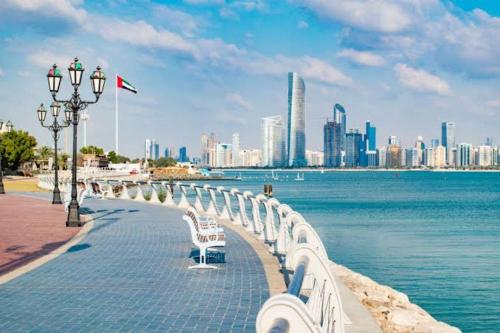 a row of white benches next to the water with a city at Orchid International in Abu Dhabi