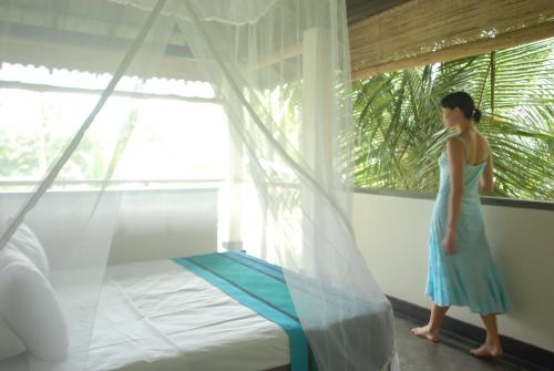 a woman in a blue dress standing next to a bed at Talalla Retreat in Talalla