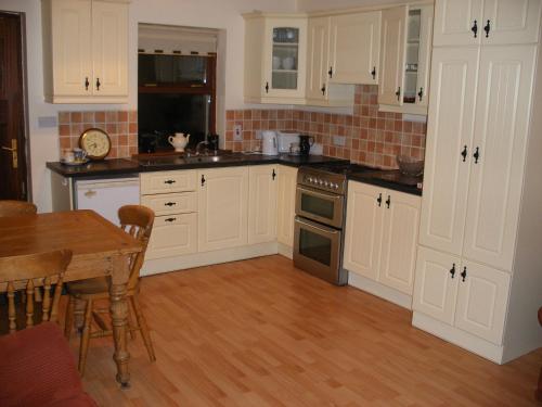 cocina con armarios blancos y mesa de madera en Mountshannon cottage, en Mountshannon