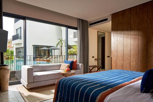 a bedroom with a bed and a couch and a balcony at Aahana Village Bali in Canggu