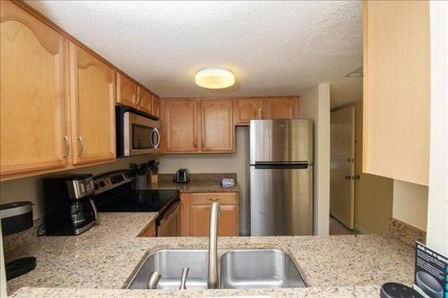 a kitchen with wooden cabinets and a stainless steel refrigerator at Mystic Sands I Steps to Beach I Free activities condo in Saint Augustine Beach