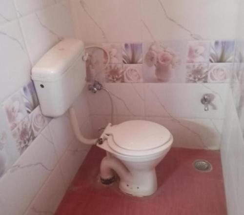 a white toilet in a bathroom with flowers on the wall at UGS guest house in Jodhpur