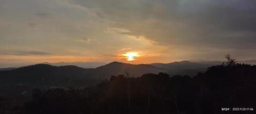 a sunset over a mountain range with the sun setting at View Point Stay in Madikeri