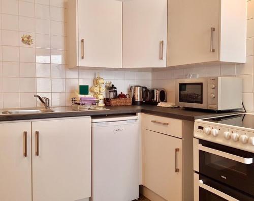 a white kitchen with white cabinets and a microwave at Harbour Street Nook in Whitstable