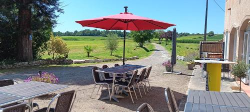a picnic table with a red umbrella and chairs at Au Moulin du Comte - en gîte in Bourrouillan