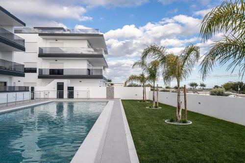 a swimming pool in front of a building with palm trees at Sunset View Apartment in Conceicao de Tavira in Tavira