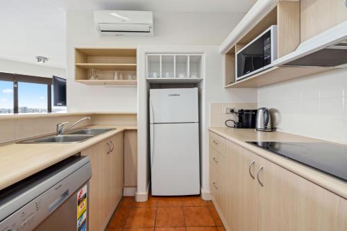 a kitchen with a white refrigerator and a sink at Tiki Hotel Apartments Surfers Paradise in Gold Coast