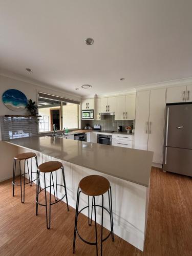 a kitchen with a large counter with three bar stools at Costa Casa Jervis Bay Retreat in Vincentia