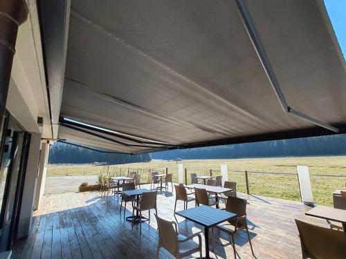 a covered patio with tables and chairs and a field at Auberge du château de Joux in La Cluse et Mijoux
