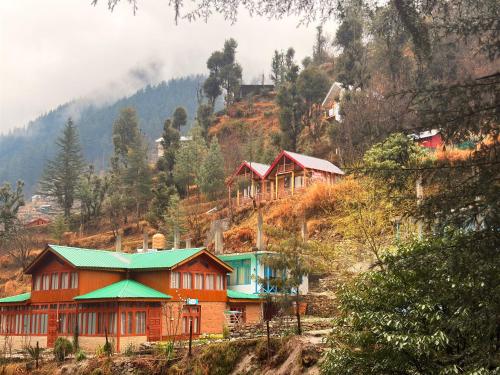 a group of houses on a hill with trees at Pine Nest cottages in Jibhi