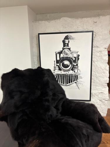 a black dog laying in front of a picture of a train at le sous sol du vétérans in Lac-Mégantic